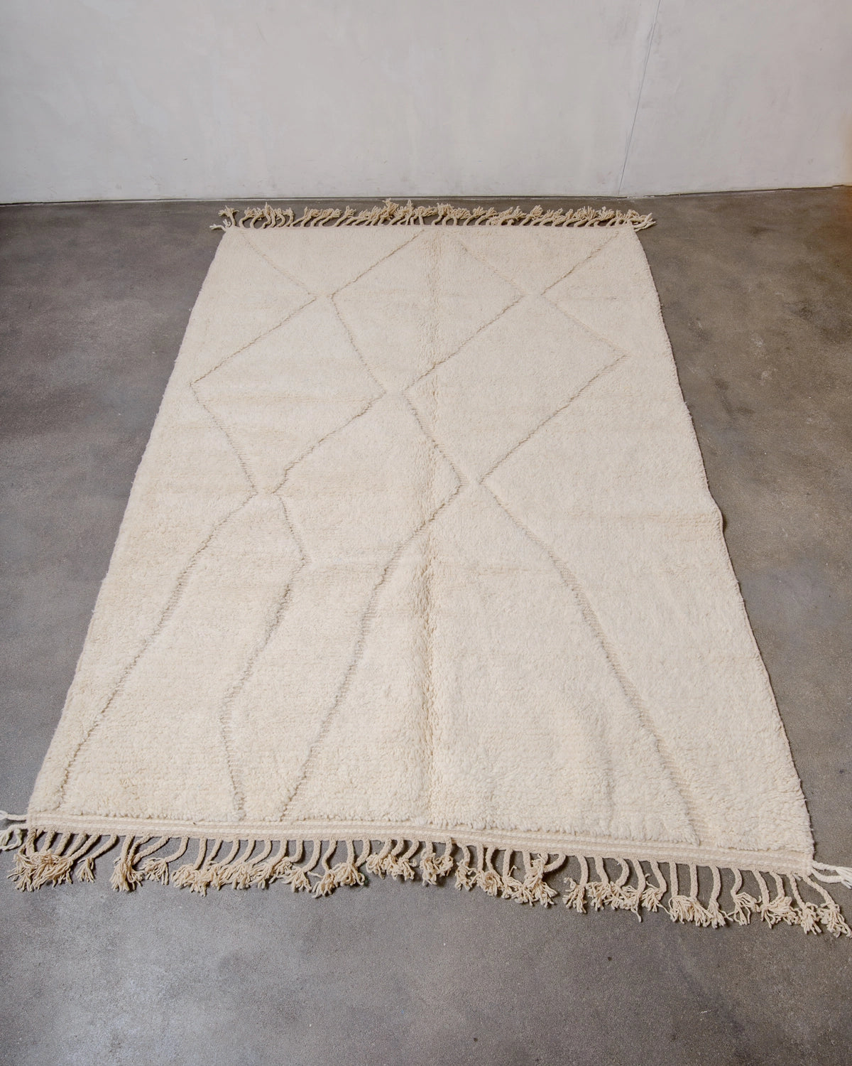 Berberlin Beniourain Rug made of natural cream wool with an abstract woven diamond design, photographed on a concrete floor.